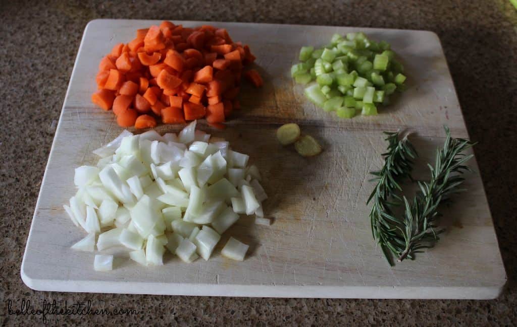 Food on a wooden cutting board, onions, carrots, celery, and garlic 