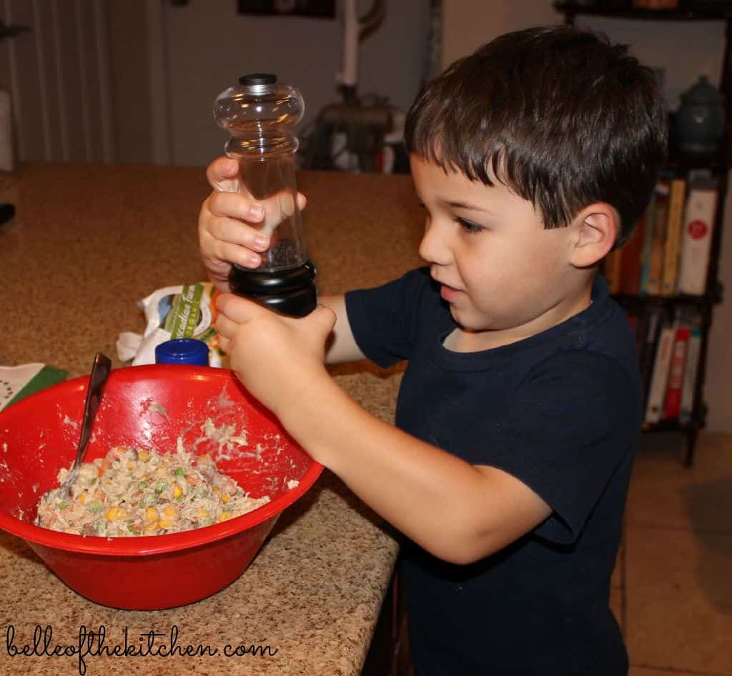 A little boy that is holding a pepper grinder over a bowl of food