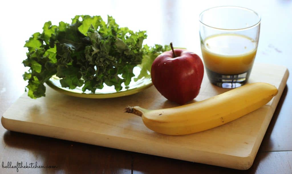 banana, apple, kale, and orange juice on a cutting board