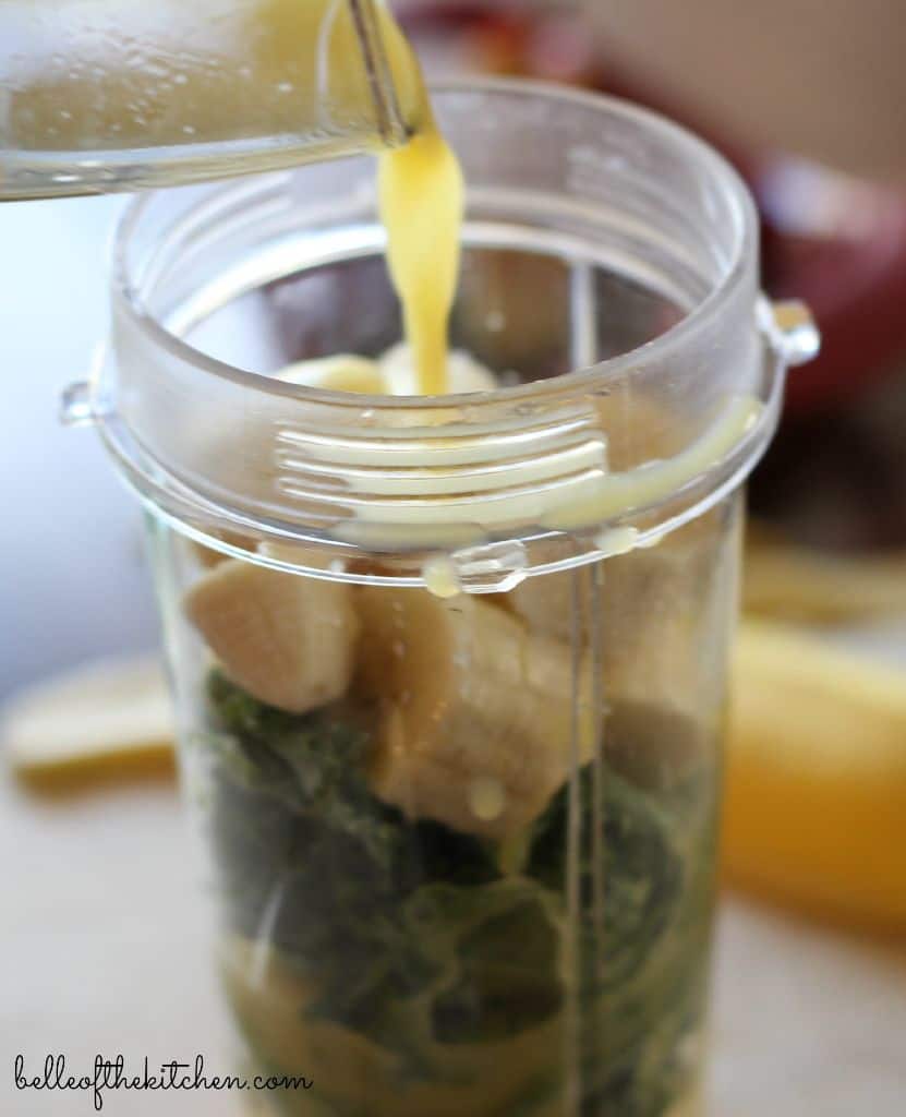 a blender jar with fruit and kale