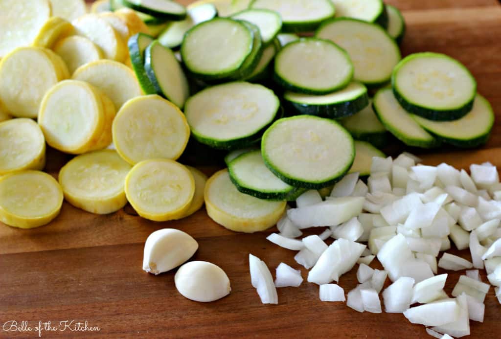 Food on a wooden cutting board, with Squash, zucchini, and onions