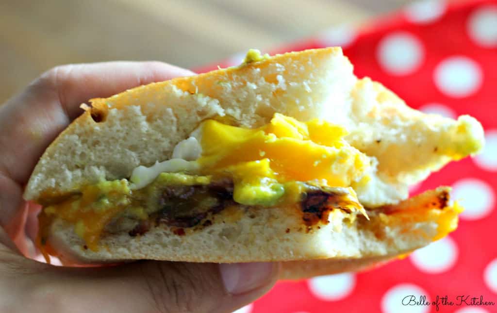 a sandwich of bacon, cheese, avocado, and egg