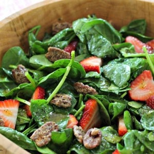 A bowl of salad, with strawberries and pecans