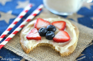 A close up of a sugar cookie topped with frosting and fruit with a bite taken out