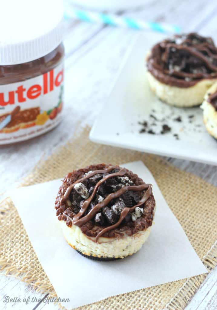 A bunch of mini cheesecakes topped with Oreos and chocolate next to a jar of Nutella 