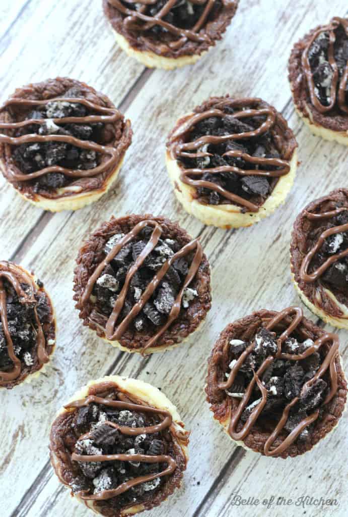 A bunch of mini cheesecakes topped with Oreos and chocolate