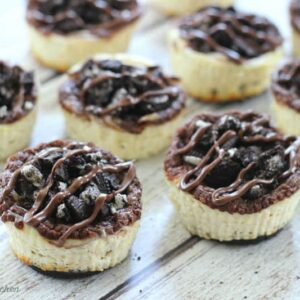 A bunch of mini cheesecakes topped with Oreos and chocolate
