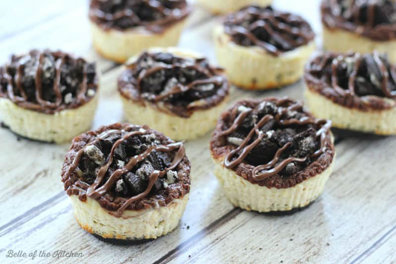 A bunch of mini cheesecakes topped with Oreos and chocolate