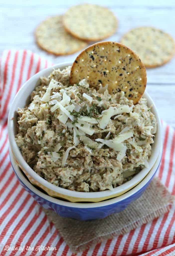 A bowl filled with tuna salad topped with cheese and a round cracker