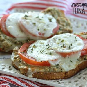 A close up of a plate of a tuna melt topped with sliced tomatoes on a plate