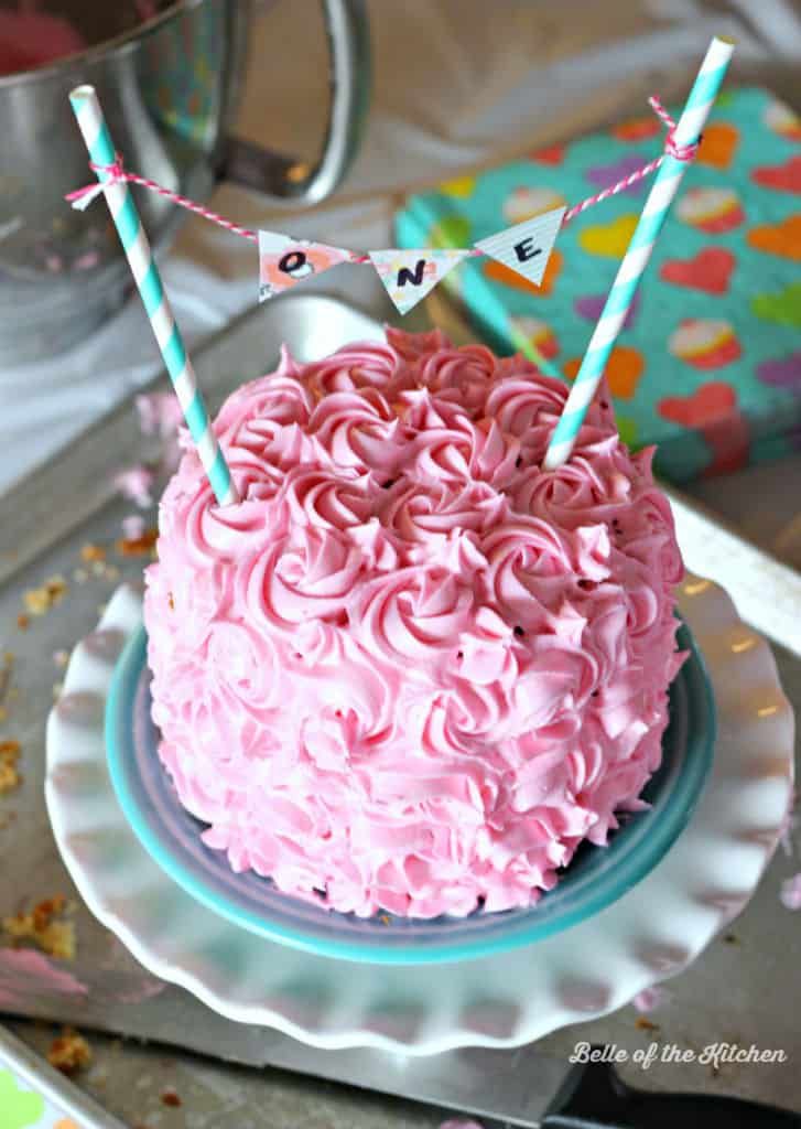 A close up of a plate with a pink frosted birthday cake