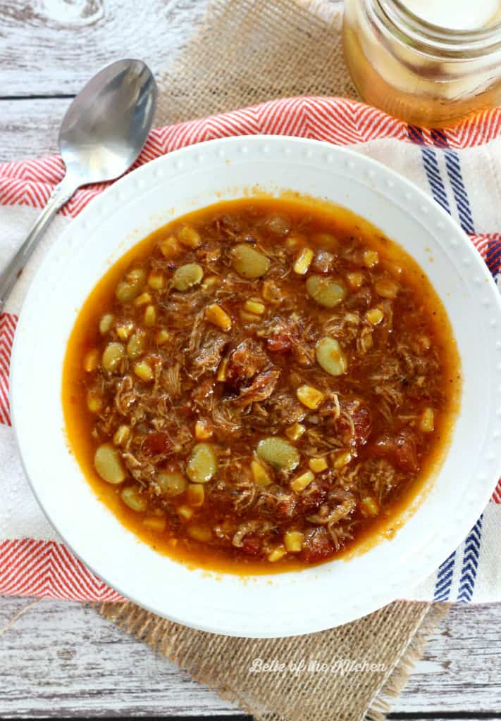 A bowl of stew with cornbread and iced tea beside it