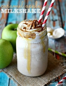 A close up of a milkshake in a mason jar beside two green apples