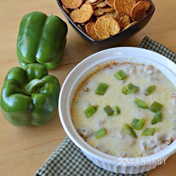 A bowl of green pepper dip on a table with a bowl of chips beside it