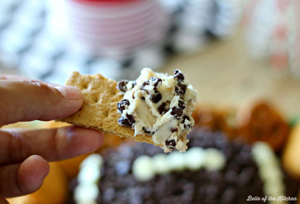 A close up of a person holding a graham cracker topped with cheeseball dip