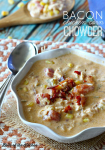 A bowl of soup topped with bacon beside two spoons
