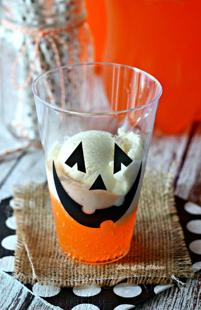 A close up of a glass with a jack o\'lantern face on the side filled with Fanta and ice cream