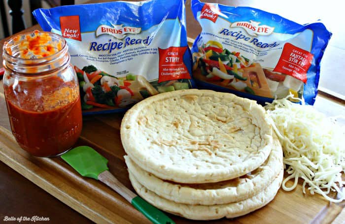 pizza crusts and bags of frozen veggies on a cutting board