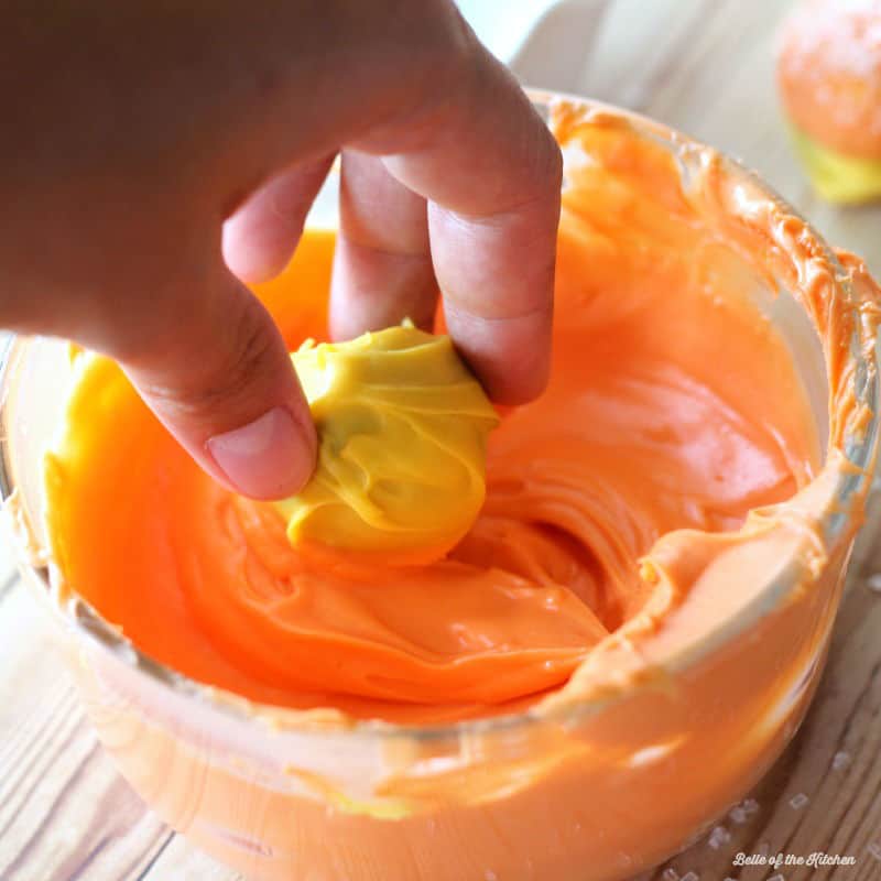 a hand dipping a cake ball in orange frosting