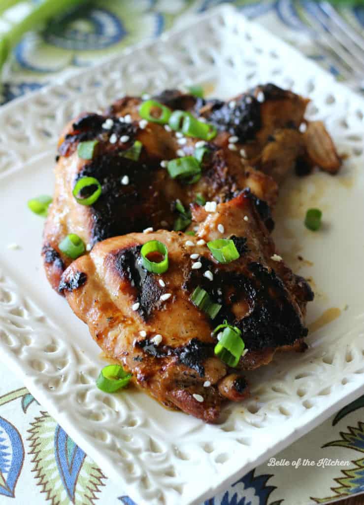 A close up of grilled chicken on a plate topped with green onions