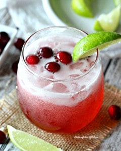 A glass of cranberry and 7Up topped with cranberries and a slice of lime