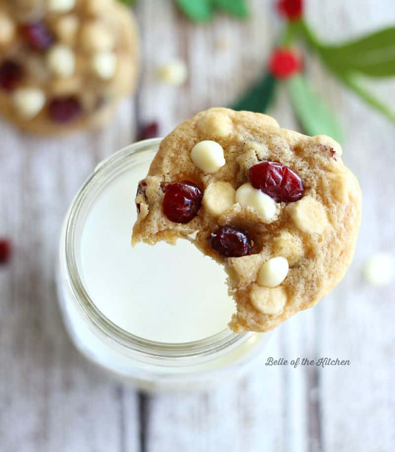 a cookie with white chocolate chips and cranberries on a glass of milk