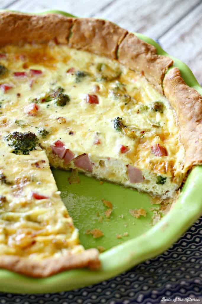 A close up of a slice of quiche in a green pie plate