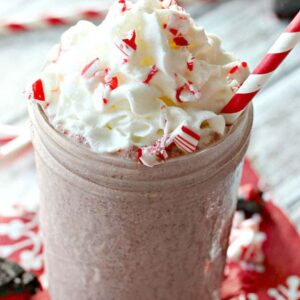 a milkshake in a mason jar topped with whipped cream, chopped peppermints, and a straw