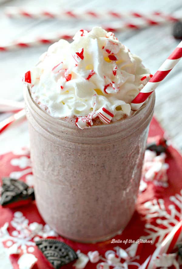 a milkshake in a mason jar topped with whipped cream, chopped peppermints, and a straw