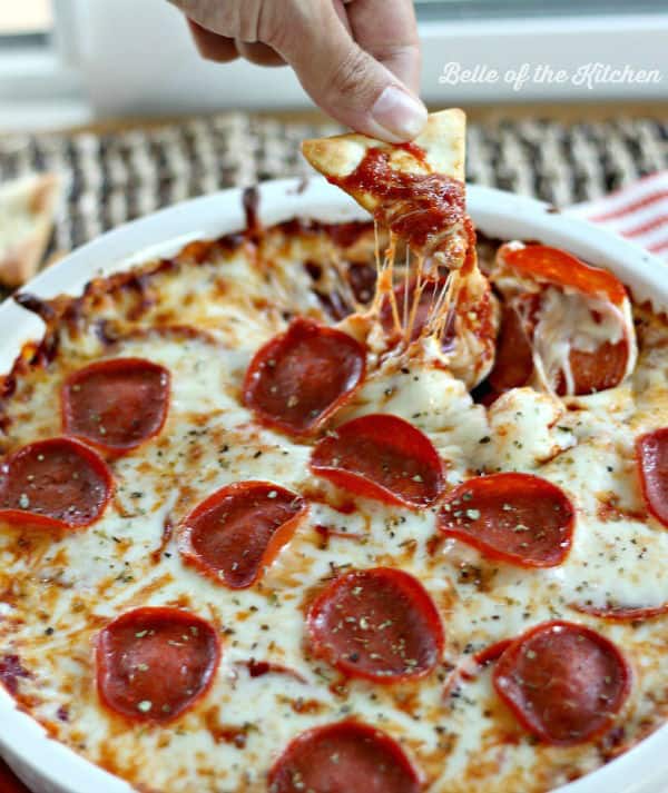 A hand dipping a chip into pepperoni pizza dip