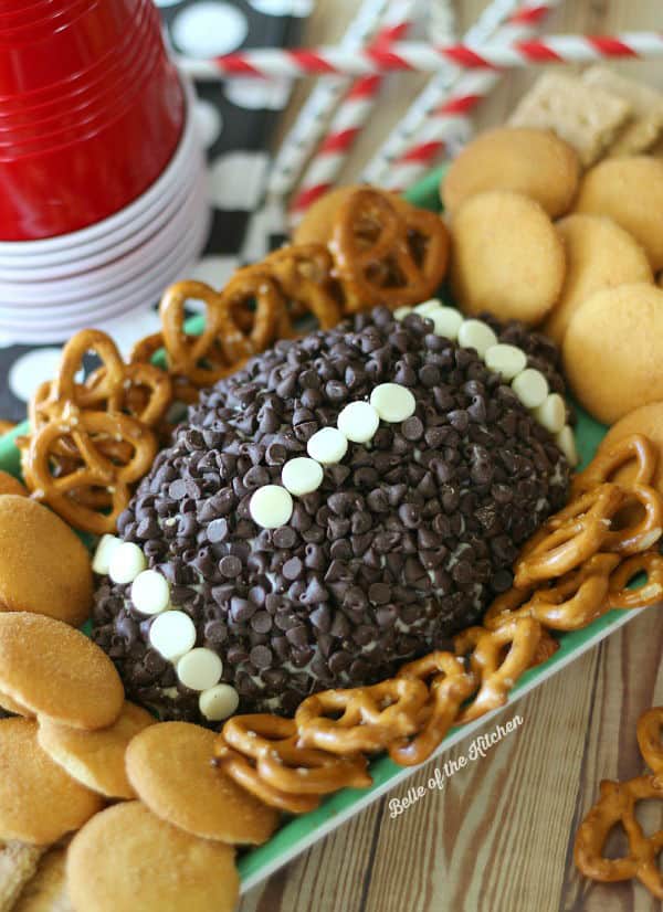 A close up of a football shaped cheeseball topped with chocolate chips and surrounded by pretzels and vanilla wafers