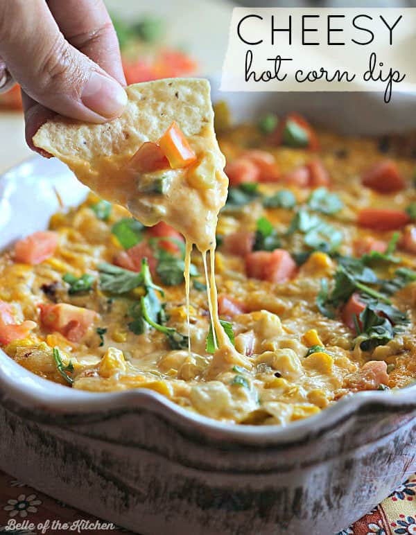 A close up of a person holding a chip dipping into hot corn dip