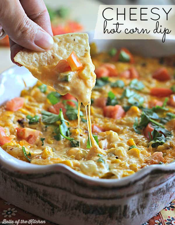 A close up of a person dipping a chip into hot corn dip
