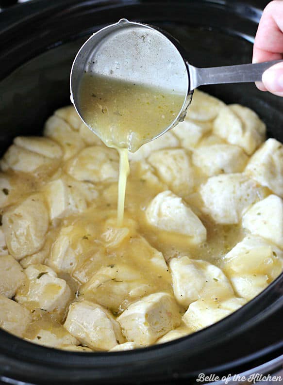 A measuring cup pouring sauce over biscuits in a crockpot
