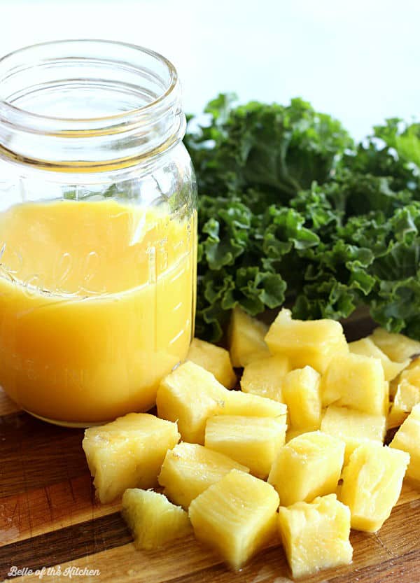 orange juice, chopped pineapple, and kale on a cutting board