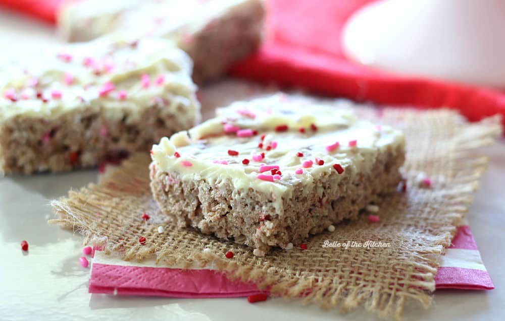 A close up of a Rice Krispie treat topped with frosting and pink sprinkles