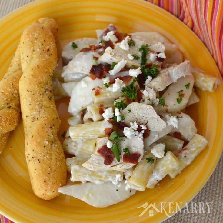 A plate of pasta with chicken and bread sticks on the side