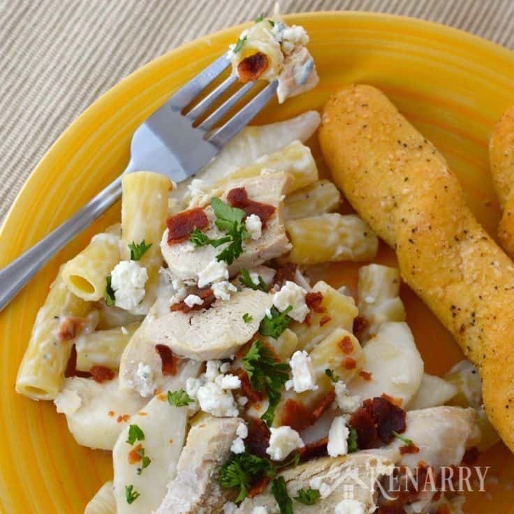 A plate of pasta with chicken and bread sticks on the side