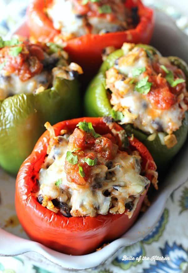 A dish is filled with peppers stuffed with a rice filling and topped with salsa and cilantro