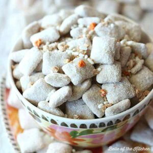 A close up of a bowl of carrot cake puppy chow topped with orange and white sprinkles