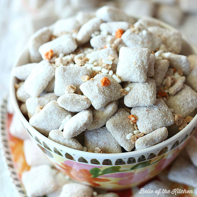 A close up of a bowl of carrot cake puppy chow topped with orange and white sprinkles