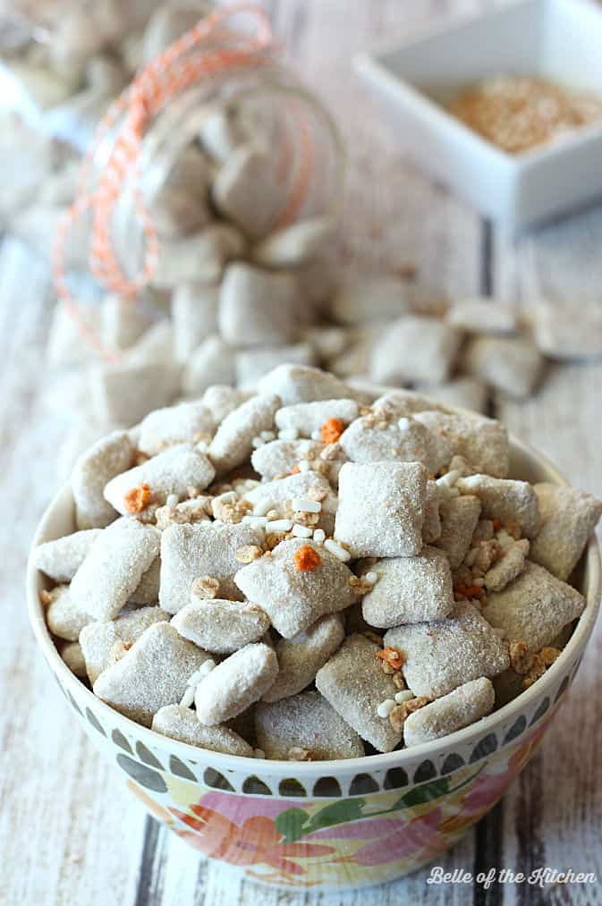 A close up of a bowl of carrot cake puppy chow topped with orange and white sprinkles