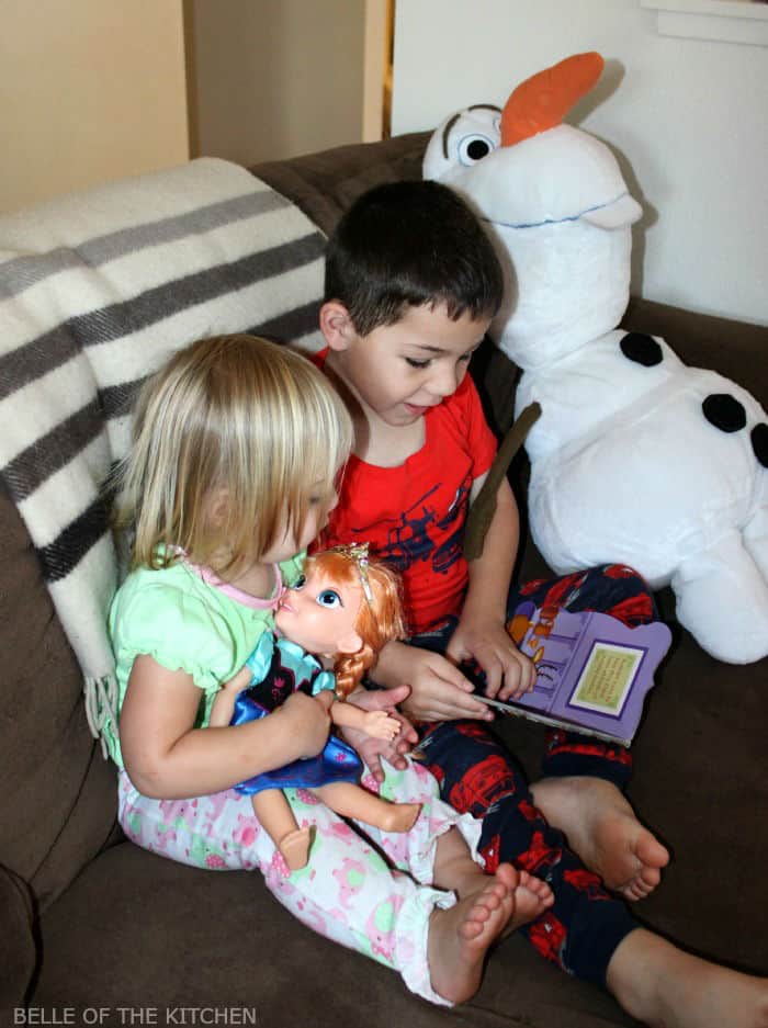 two kids sitting on a couch reading a book together