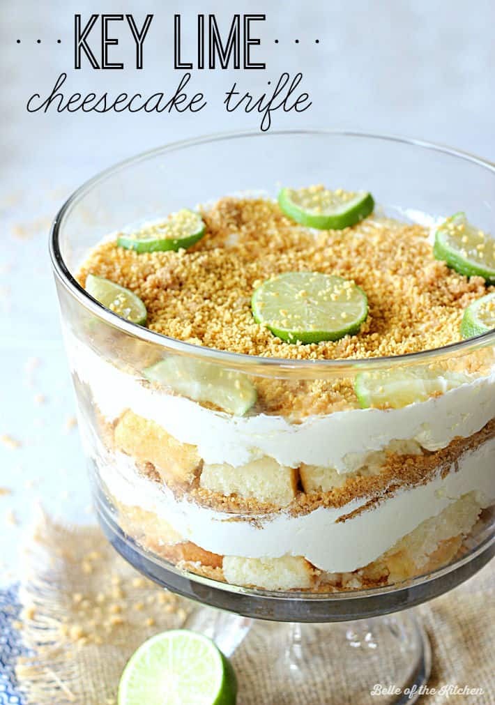 A close up of a trifle dish filled with layers of cheesecake filling, chopped pound cake, and topped with graham cracker crumbs and sliced lime