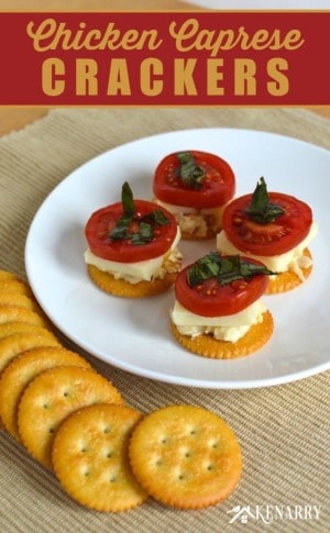 A plate of crackers topped with cheese, chicken, and sliced tomato