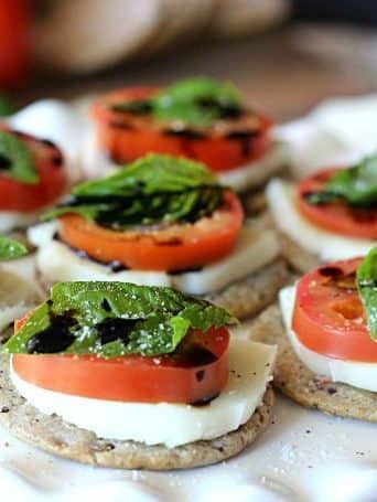 crackers topped with sliced tomato, mozzarella, basil, and balsamic glaze
