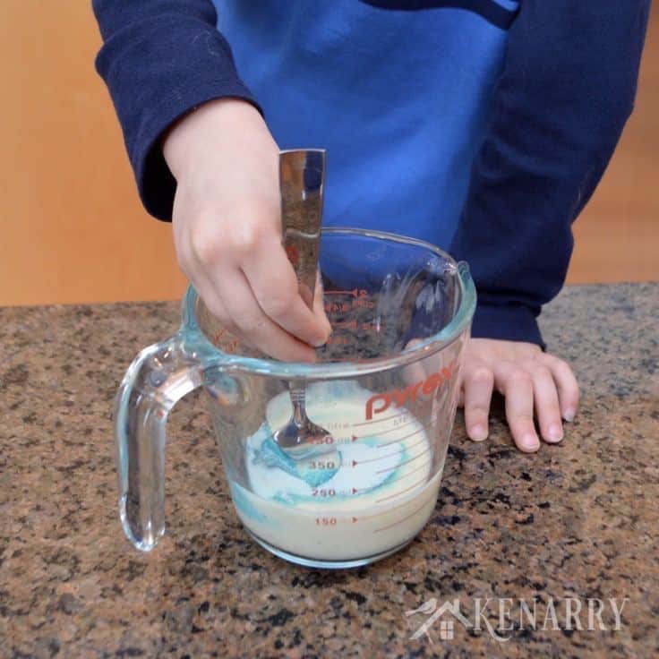 a person mixing food coloring into a liquid glass measuring cup