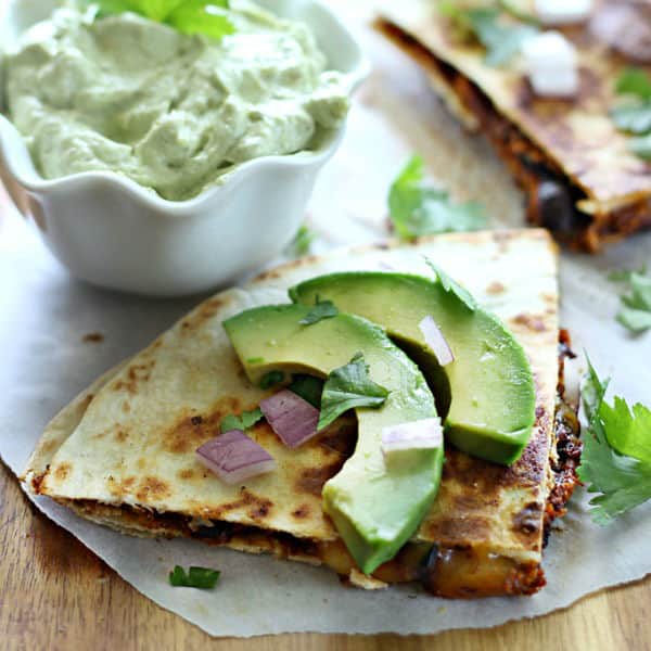 A close up of a slice of a Quesadilla next to a bowl of avocado cream