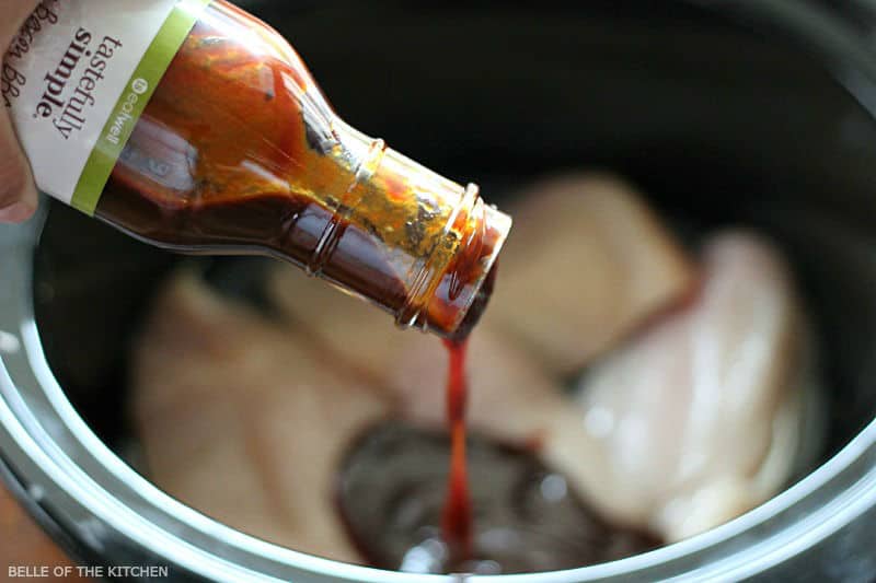 bbq sauce being poured over chicken in a crockpot