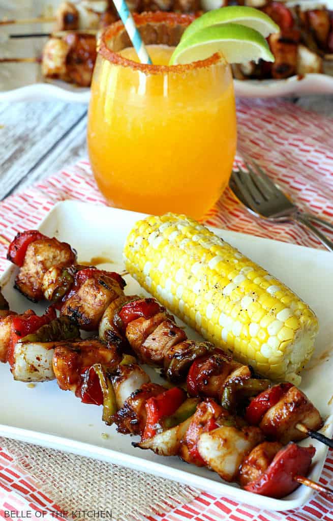 A plate of food on a table, with Chicken skewers and grilled corn